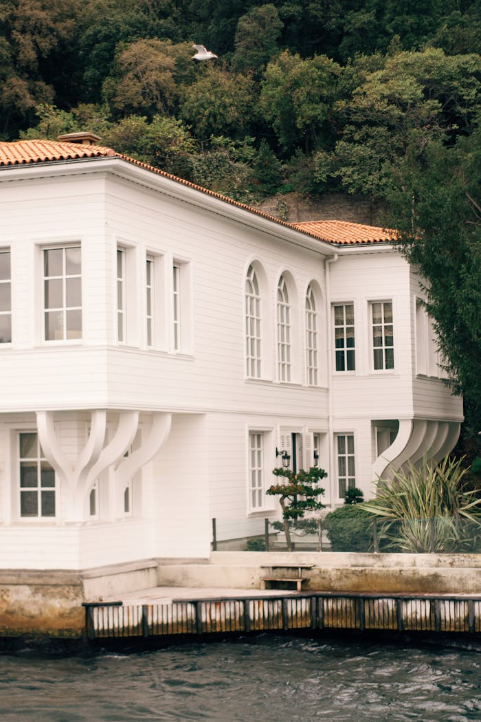 Stunning white house by the water with lush greenery, showcasing elegant architecture.